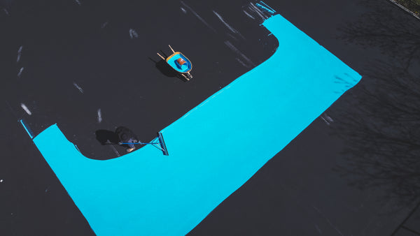 Painting the inside area of a backyard tennis court with Laykold Light Blue.