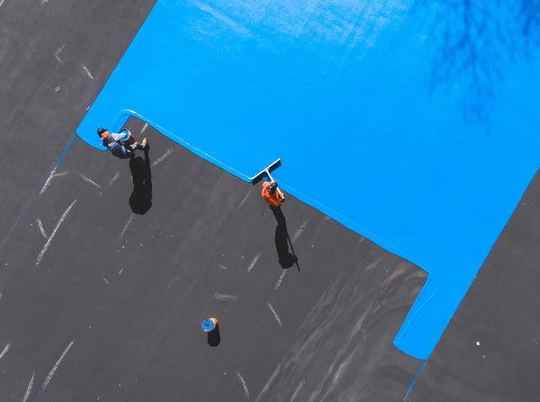 Applying Laykold Dark Blue acrylic color coating to the inner playing area of a tennis court after completed acrylic resurfacer.