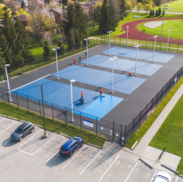 Applying the second coat of Laykold Dark Blue on a public tennis court.